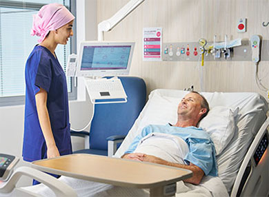 A nurse talking to a patient in a bed in hospital